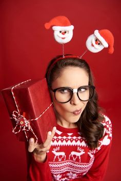 a woman wearing glasses and holding a red present box with santa hats on her head