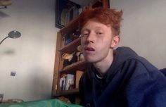 a young man with red hair is sitting on a bed and looking at the camera