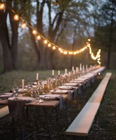 a long table is set with candles and place settings for an outdoor dinner in the woods