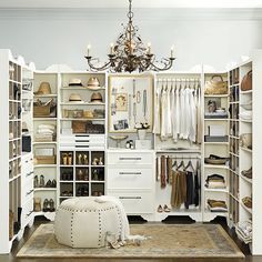 an organized closet with white furniture and chandelier