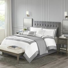 a bed with white and grey comforters in a room