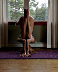 a woman is doing yoga in front of a window with her hands behind her head