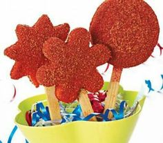 two red heart shaped lollipops sitting in a yellow cup filled with candy