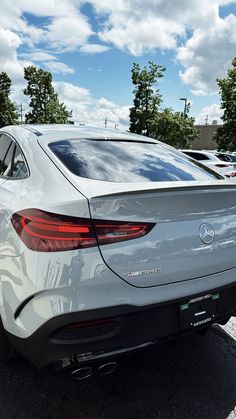 the rear end of a white car parked in a parking lot with other cars behind it