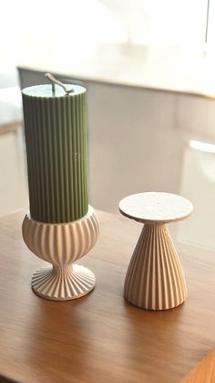 two vases sitting on top of a wooden table next to each other, one green and the other white