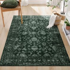 a green area rug with an ornate design on the floor and wooden chairs around it