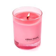 a pink candle is sitting in a clear glass container on a white background with the word glitter bomb written below it