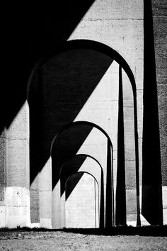 black and white photograph of an arch between two concrete pillars with long shadows on the wall