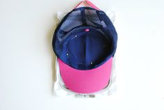 a pink and blue hat sitting on top of a plastic bag next to a white wall