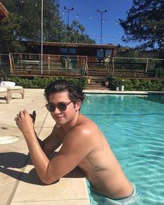 a shirtless man sitting in the middle of a swimming pool with sunglasses on his head