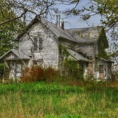 an old house sitting in the middle of a field with tall grass and trees around it