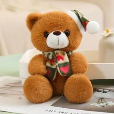 a brown teddy bear wearing a santa hat and scarf sitting on top of a magazine