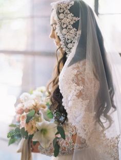 a woman in a wedding dress holding a bouquet with flowers on the side and veil over her head