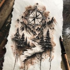 a drawing of a compass on paper with trees and mountains in the background, surrounded by watercolor pencils