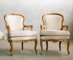 two white chairs sitting next to each other in front of a gray wall with gold trim