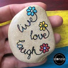 a hand holding a rock with the words live love laugh painted on it and flowers