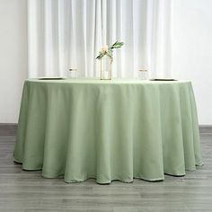 a round table with two vases on it in front of a curtained window