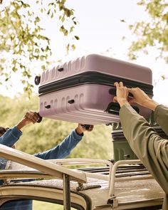 two people holding up a purple piece of luggage