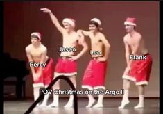 three men in santa hats and red trunks are standing on stage with their arms up