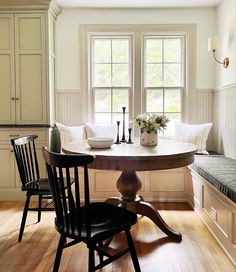 a kitchen table with two chairs and a bench in front of the window, next to an entryway