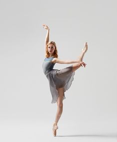 a young ballerina is posing for the camera in her dance studio, wearing a gray dress and ballet shoes