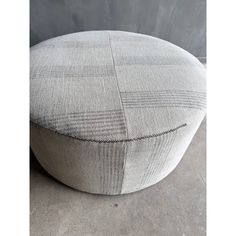 a grey and black checkered round ottoman on concrete floor with gray wall in the background