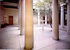 an empty building with columns and trees in the center, surrounded by white pillars on either side