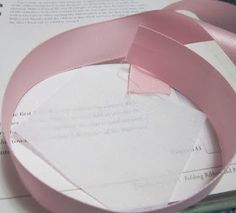 a pink ribbon is laying on top of some papers