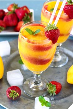 two glasses filled with fruit on top of a metal tray next to lemons and strawberries