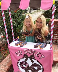 two girls standing behind a pink and white ice cream cart with donuts on it