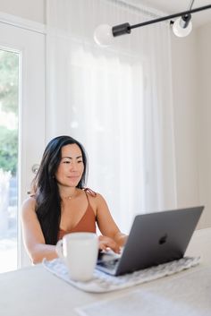 a woman sitting at a table with a laptop computer in front of her and a cup of coffee