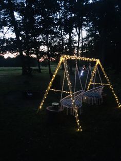 a swing set with lights on it in the dark, surrounded by trees and grass