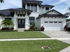 a large white house with black roofing and palm trees in the front yard area