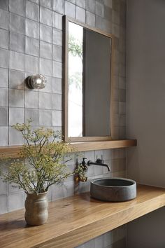 a bathroom sink sitting under a mirror next to a vase with flowers on top of it