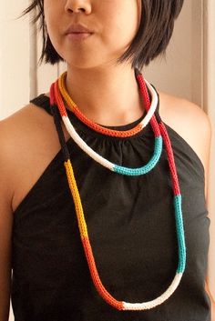 a woman wearing a multicolored necklace and black tank top standing in front of a door