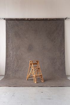 a wooden chair sitting on top of a cement floor next to a ladder in front of a wall