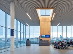 an airport terminal with people sitting in chairs and looking out the windows at planes on the tarmac