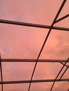 the sky is pink and cloudy as seen from inside a metal structure at an airport