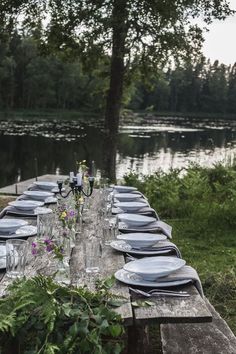 a long table set with plates and silverware on it in front of a lake