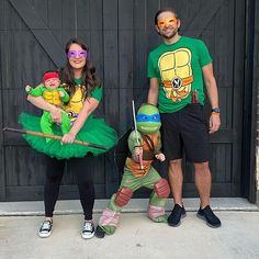 two adults and one child dressed up in teenage mutant costumes, standing next to each other