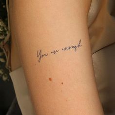 a woman's arm with the words you are enough written in cursive ink