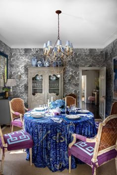 a dining room table with blue and purple chairs in front of a chandelier