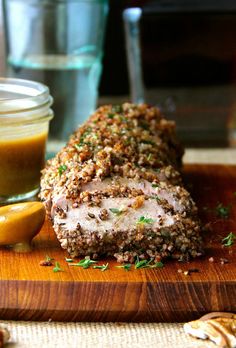 a wooden cutting board topped with meat covered in seasoning next to a jar of mustard