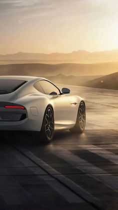 a white sports car driving on a road near the ocean at sunset or sunrise time