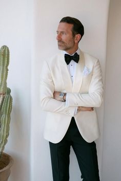 a man in a tuxedo leaning against a wall next to a cactus plant