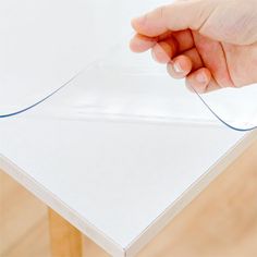 a hand is holding the edge of a piece of white paper on top of a wooden table