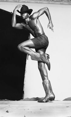 a black and white photo of a man in cowboy boots posing on stage with his hands behind his head