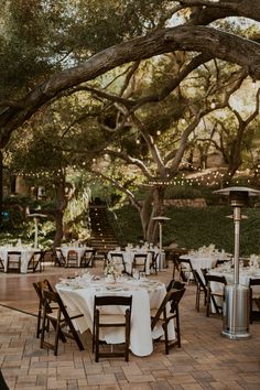 an outdoor dining area with tables and chairs set up for dinner under the tree's branches