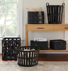 three black baskets sitting on top of a wooden shelf in front of a window next to a bookshelf