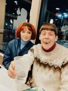 two people sitting at a table with drinks in front of them and one person holding a cup